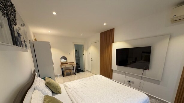 Un dormitorio con una cama, un televisor montado en la pared y un escritorio con una silla.