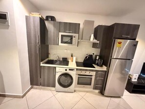 Ett kompakt kök med inbyggd tvättmaskin, mikrovågsugn, spis och kylskåp.
