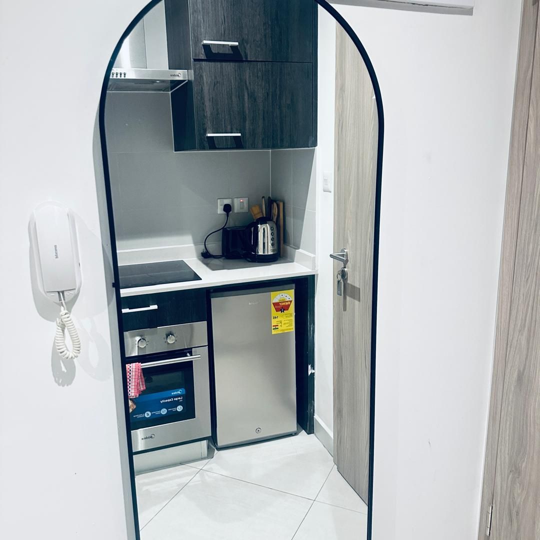 Una kitchenette compacta con horno integrado, un refrigerador pequeño, un tostador y un teléfono.