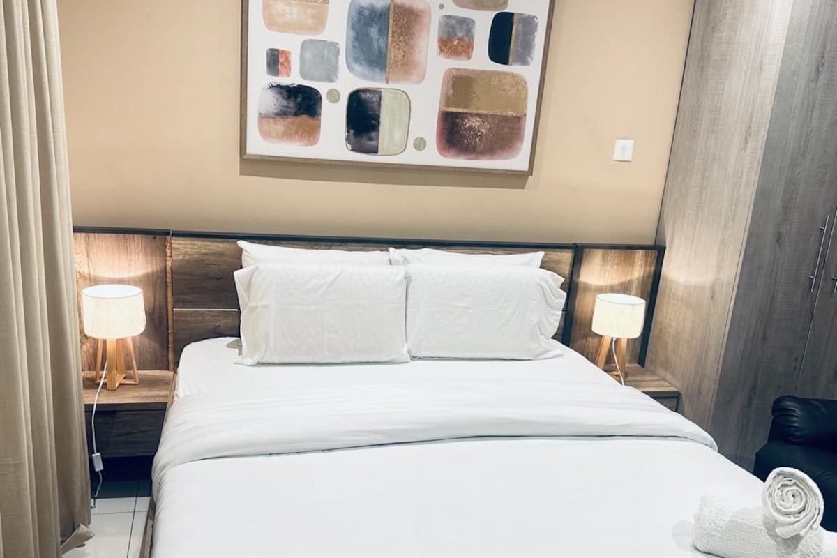 Ett hotellrum med en säng, två sänglampor, en stor abstrakt målning på väggen och en garderob.