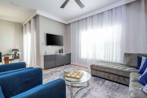 Ein modernes Wohnzimmer mit einem Flachbildfernseher, einem grauen Sofa, blauen Sesseln und einem Glastisch.