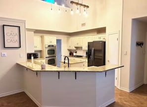 Une cuisine moderne dotée d’un îlot central, d’appareils électroménagers intégrés et d’un luminaire suspendu.