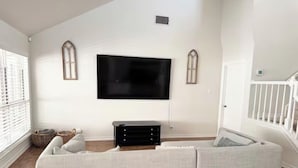 A living room with a sectional sofa, a flat-screen TV mounted on the wall, and a staircase to the right. - The Berg - 5 min. From Six Flags, La Cantera & the Rim (San Antonio)