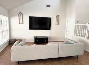Un salon avec un canapé d’angle, un téléviseur à écran plat fixé au mur et un escalier sur le côté droit.