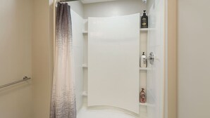 Et brusebad med håndklædetørrer, bruseforhæng og en hylde med toiletartikler.