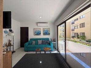A modern living room with a teal sofa, a coffee table, and a TV mounted on the wall. - Oceanna | Pools, Rooftop with Jacuzzi and BBQ Area (Mazatlán)