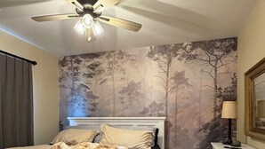 Un dormitorio con una cama, un ventilador de techo, un tocador y una pared con un mural de un árbol.