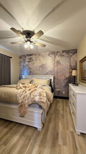 Una camera da letto con un letto, una ventola a soffitto, una cassettiera e una parete con un affresco di alberi.