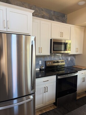 A modern kitchen with stainless steel appliances, white cabinetry, and a marble backsplash.