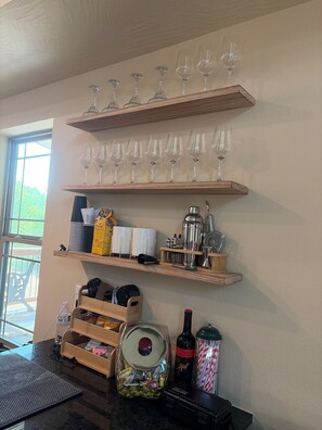A kitchen with wooden shelves holding wine glasses, kitchen utensils, and a coffee machine.