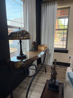 A room with a table lamp, a wooden box, a bear figurine, and a window with curtains.