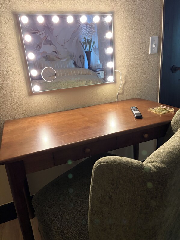 Une pièce comprenant une coiffeuse avec miroir et éclairage, un bureau en bois et une chaise.