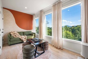 Ein modernes Wohnzimmer mit einem grünen Sofa, einem Couchtisch und Blick auf einen Wald durch große Fenster.