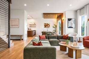 Un salon moderne avec un canapé d’angle, un coin repas et une cuisine en arrière-plan.