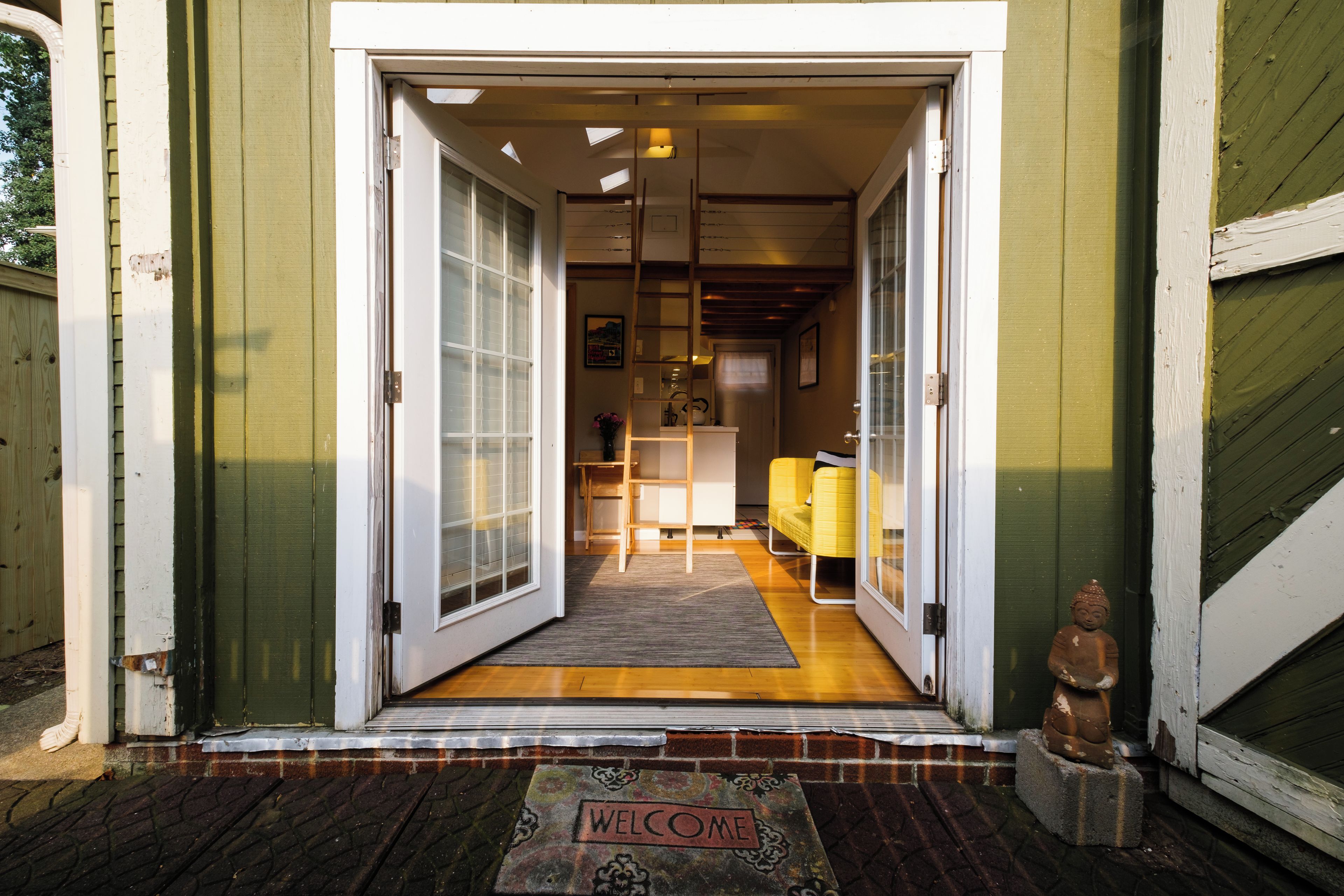 A wooden door with a welcome mat, a yellow chair, and a small statue outside a building.