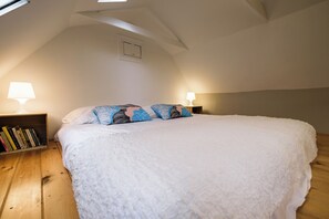 Ein Schlafzimmer mit einem großen Bett, einem Nachttisch, einem Bücherregal und einem Oberlicht.