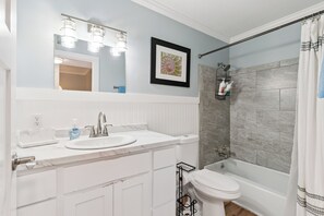 Une salle de bain avec un lavabo blanc, un miroir avec éclairage intégré, des toilettes et un espace douche.