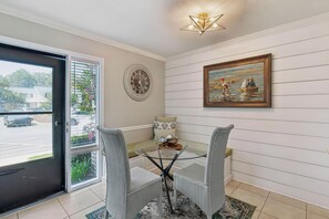 A dining area with a glass table, wicker chairs, a clock, and a painting on the wall. - Shore Thing- 2 Bed, 2.5 Bath Condo (St. Simons Island)