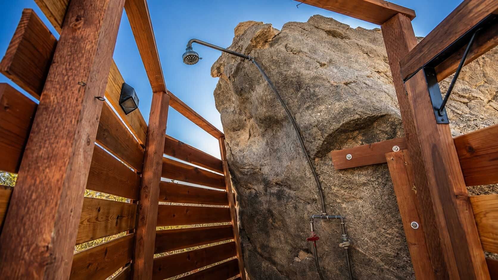 Un escalier en bois menant à une formation rocheuse sur laquelle est fixée une pomme de douche.