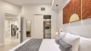Een moderne slaapkamer met een bed, nachtkastjes, een kledingkast en een badkamer zichtbaar door een geopende deur.