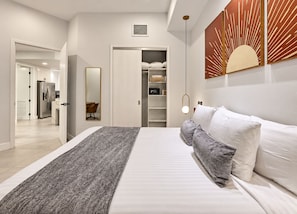 A modern bedroom with a bed, bedside tables, a wardrobe, and a bathroom visible through an open door. - Ocean-View Las Palomas 9th floor 1BR  Luxury Condo Phase II Closest to Beach (Puerto Peñasco)