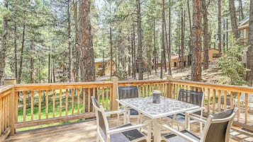 Een houten terras met een tafel en stoelen, omringd door hoge bomen en uitzicht op chalets.