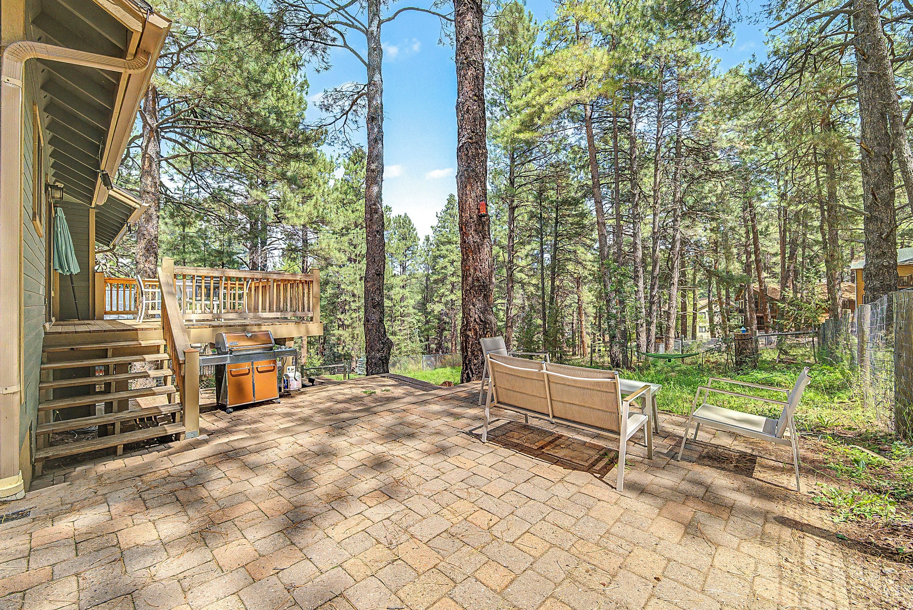 Eine Holzterrasse mit Grill, Sitzgelegenheiten im Freien und Blick auf eine bewaldete Gegend.