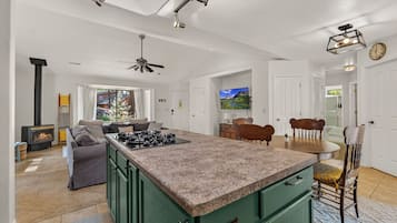 Een ruime keuken met een centraal eiland, een eethoek met een houten tafel en stoelen, en een zithoek met een bank en een open haard.