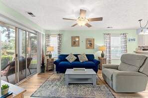 Ein Wohnzimmer mit einem blauen Sofa, einem grauen Sessel, einem Deckenventilator und einem Couchtisch.