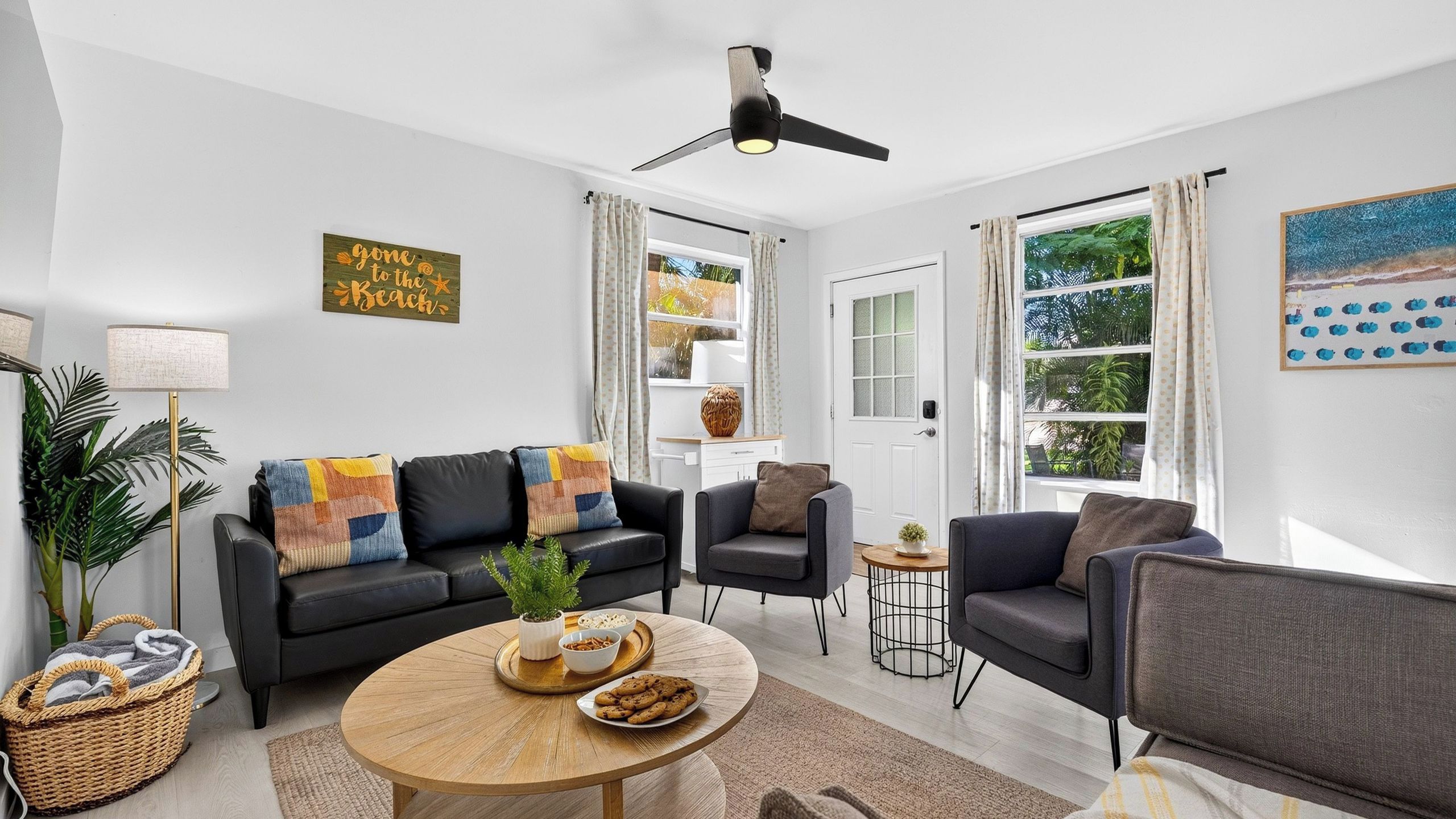 A modern living room with a black leather sofa, a round wooden coffee table, and a ceiling fan.