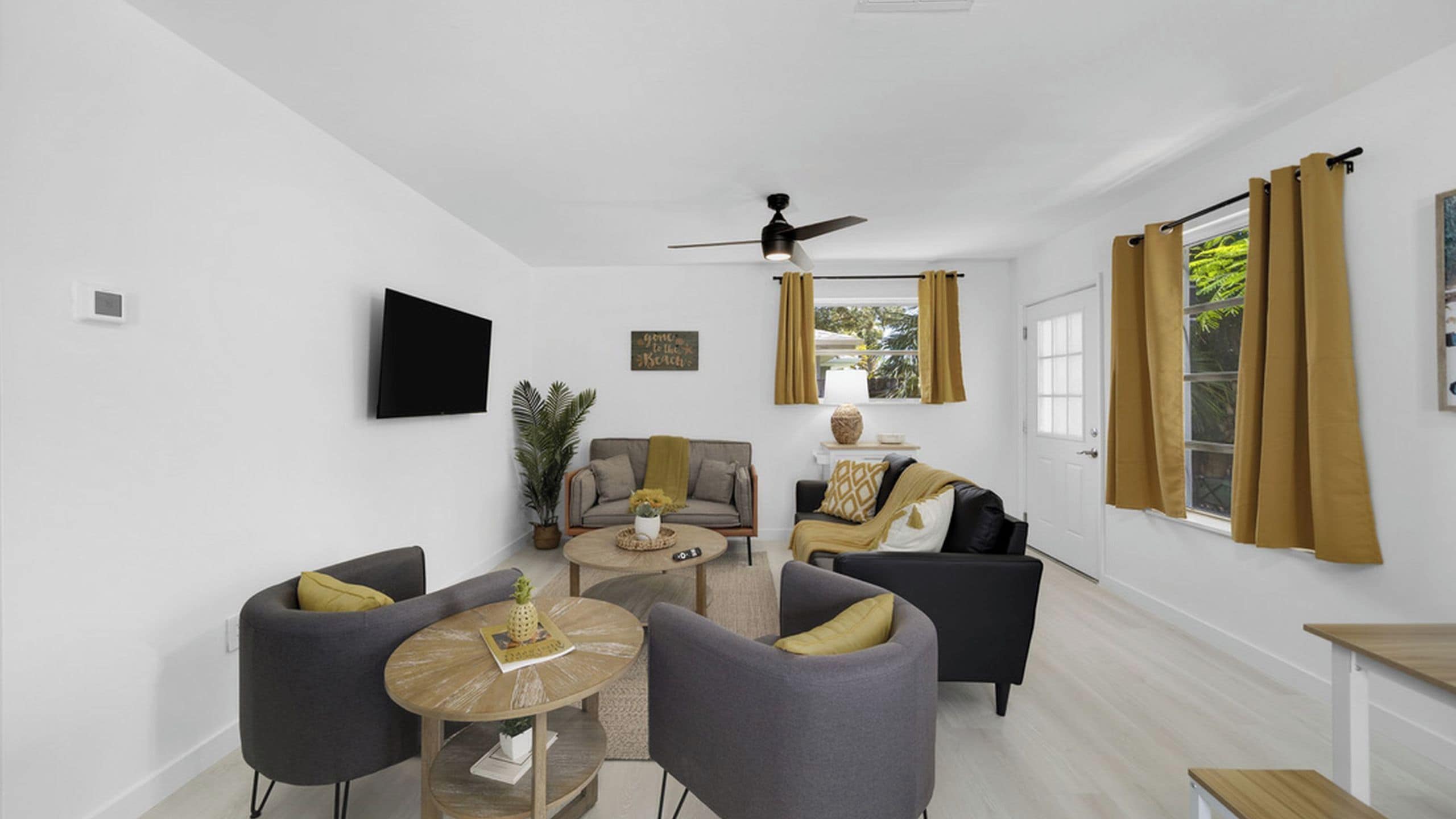 A modern living room with a flat-screen TV, a ceiling fan, and a large window with curtains.