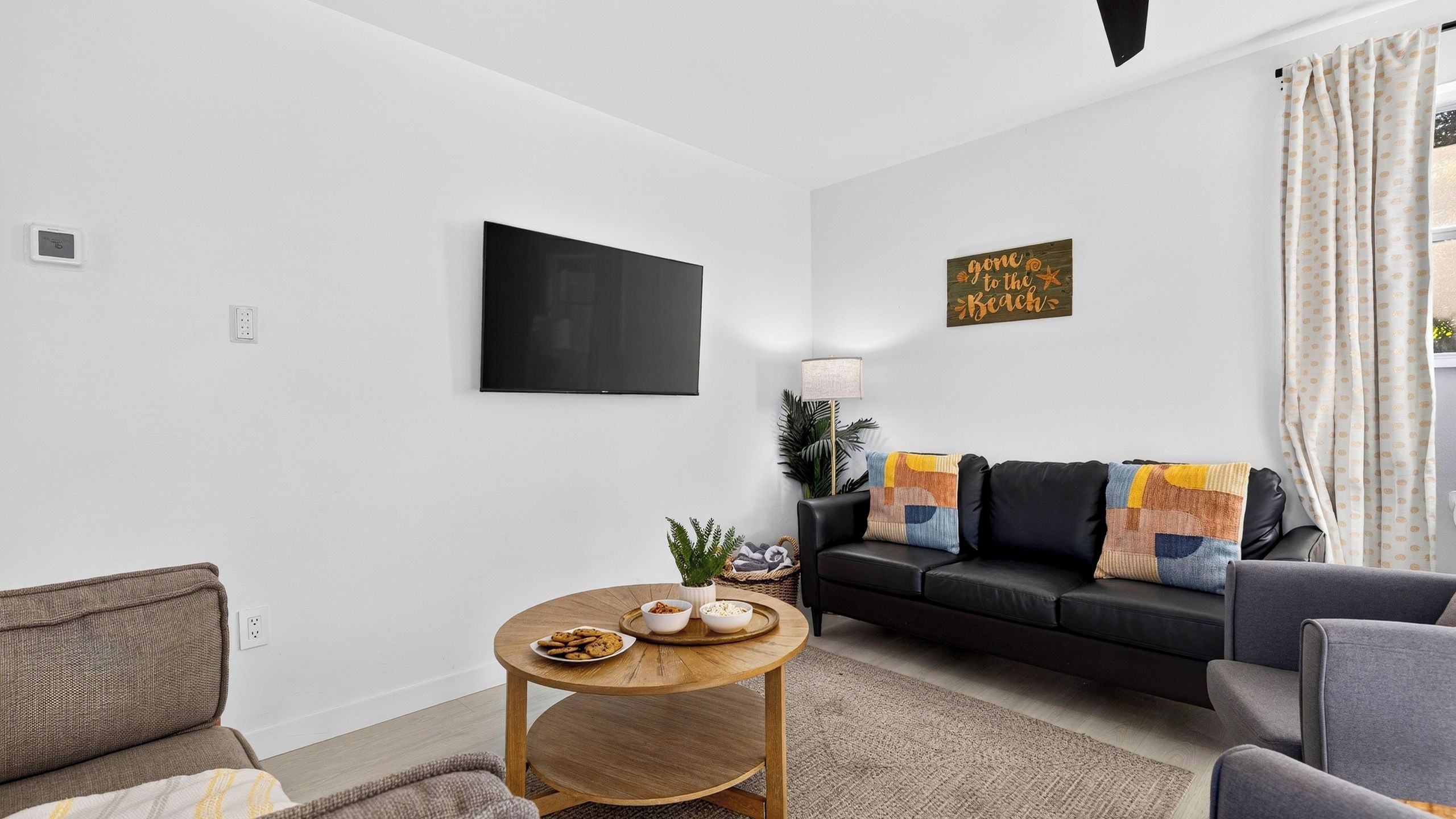 Ein modernes Wohnzimmer mit einem Flachbildfernseher, einem Sofa mit Stranddeko, einem Couchtisch mit Snacks und einer kleinen Pflanze.