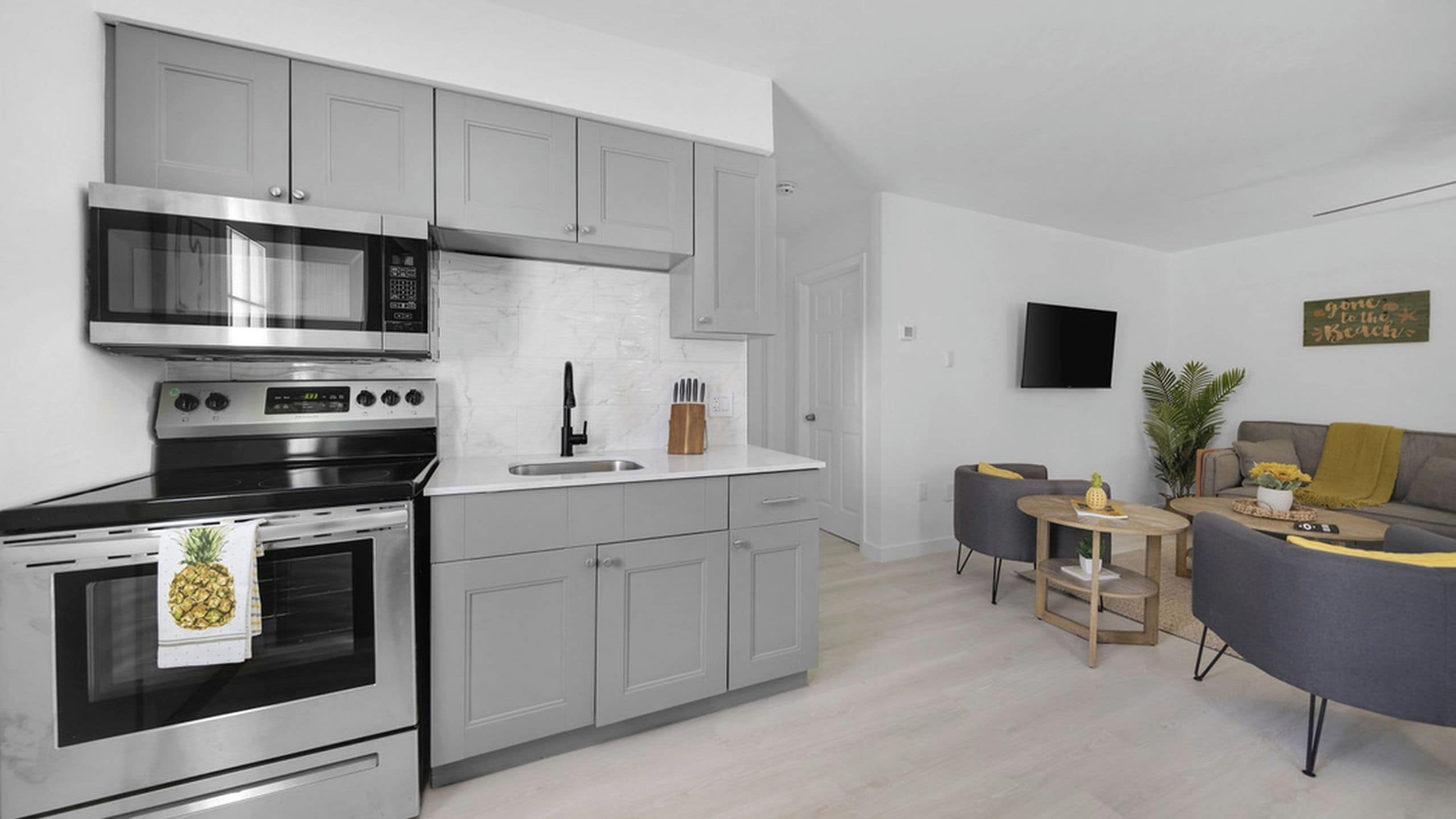 A modern kitchen with stainless steel appliances, a white tiled backsplash, and grey cabinetry.