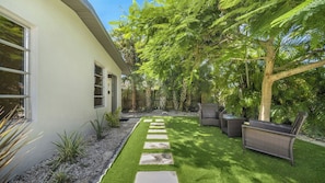 Ein modernes Haus mit gepflasterter Terrasse, Gartenmöbeln und üppiger Bepflanzung.