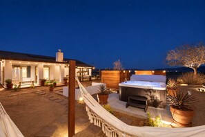 A well-lit outdoor patio area with a hot tub, seating, and potted plants. - Sun Mesa Sanctuary · Pickleball, Pool, Sauna (Joshua Tree)