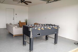 A room with a foosball table, a sofa, and a ceiling fan. - Sun Mesa Sanctuary · Pickleball, Pool, Sauna (Joshua Tree)