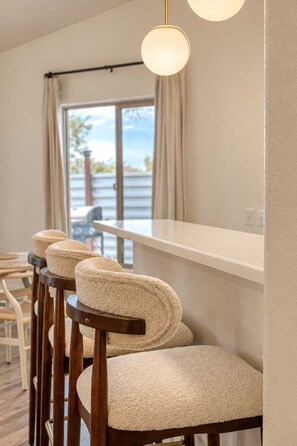 A bar area with wooden chairs and a white counter. - Sun Mesa Sanctuary · Pickleball, Pool, Sauna (Joshua Tree)