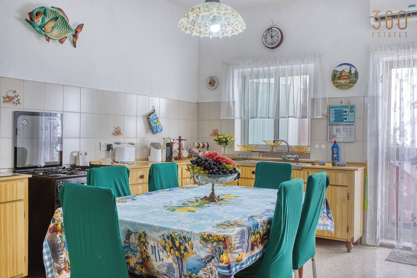 A kitchen with a dining area, featuring a stove, a sink, and a clock on the wall.