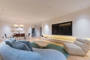 A modern living room with a sofa, a dining area, and a TV mounted on the wall. - Maison BE Residences (Lagos)