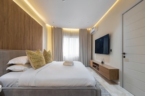A modern bedroom with a large bed, a TV mounted on the wall, and a wooden wardrobe.