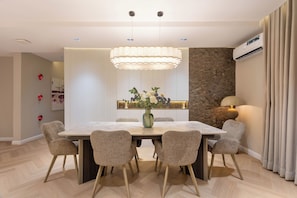 A modern dining room with a rectangular table, six chairs, a central vase with flowers, a pendant light, and a wall-mounted air conditioner.