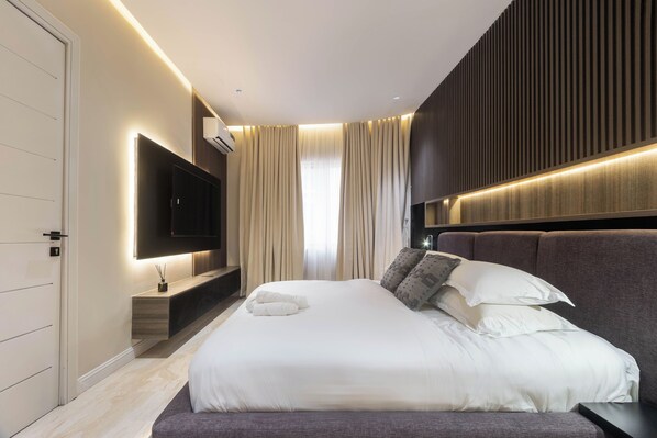 A modern bedroom with a large bed, a flat-screen TV mounted on the wall, and a wooden bedside table.