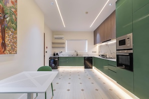 A modern kitchen with green cabinets, a white countertop, and a dining area with a white table.