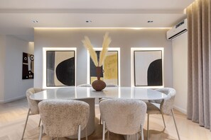 A modern dining room with a round table, six chairs, and three abstract paintings on the wall. - Maison BE Residences (Lagos)