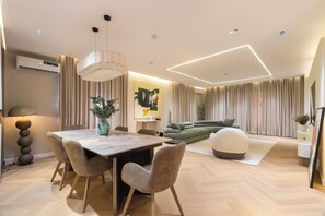 A modern living room with a dining area, featuring a large table, chairs, a sofa, and a decorative lamp.