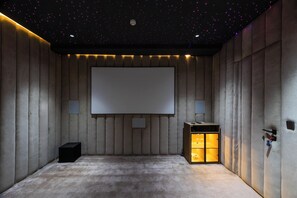 A room with a large screen, cushioned walls, a carpeted floor, and a small cabinet with a light.