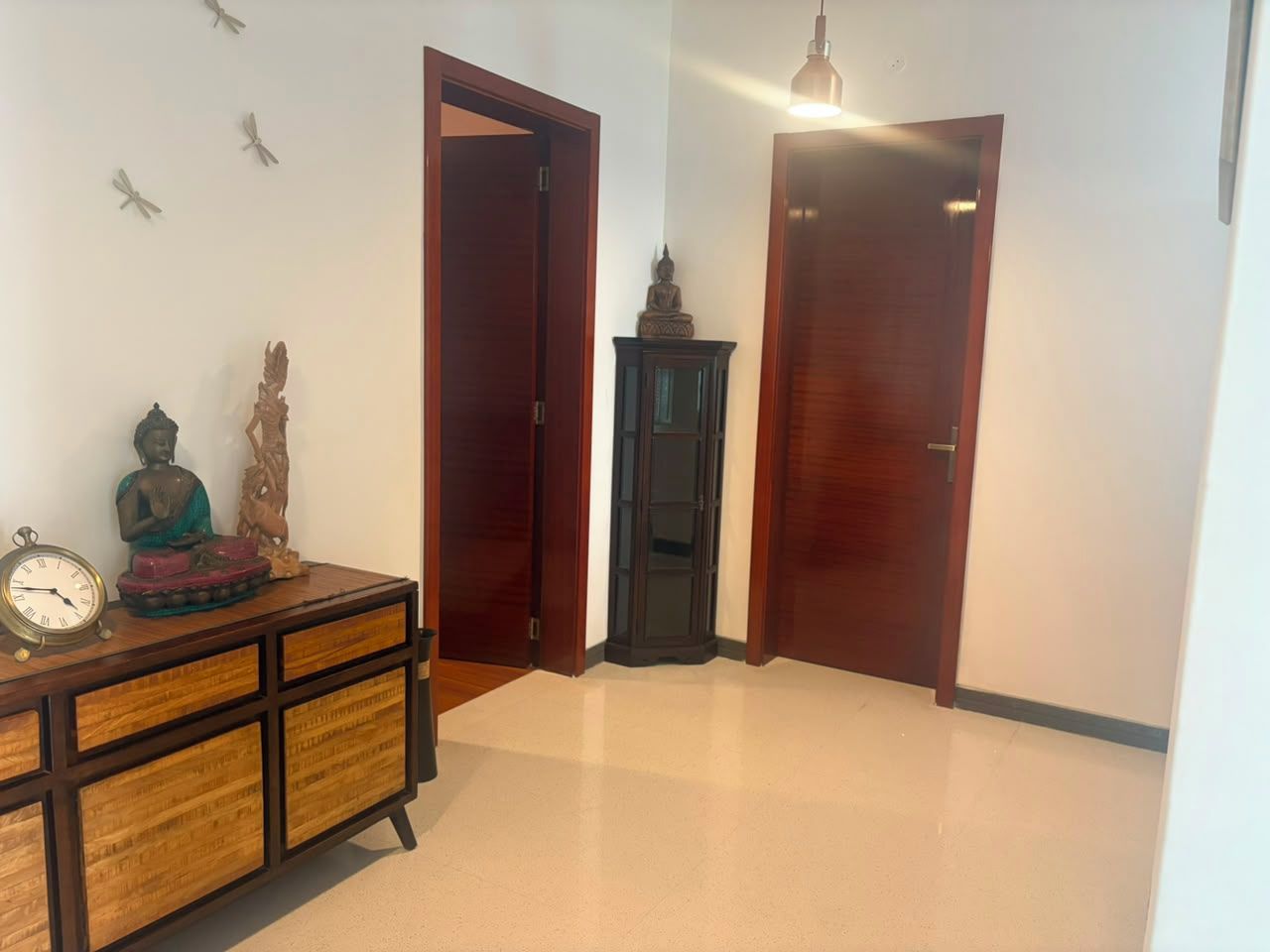 A hallway with wooden doors, a clock, and a cabinet with decorative items.