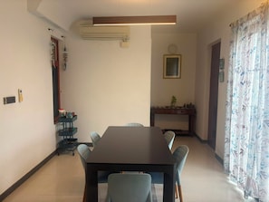 A dining area with a rectangular table and four chairs, an air conditioning unit, a small console table with a plant, and a door with a mirror. - Optimus stay'z (Tirupporur)