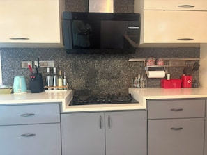 A kitchen with a gas stove, a microwave, and a patterned backsplash. - Optimus stay'z (Tirupporur)