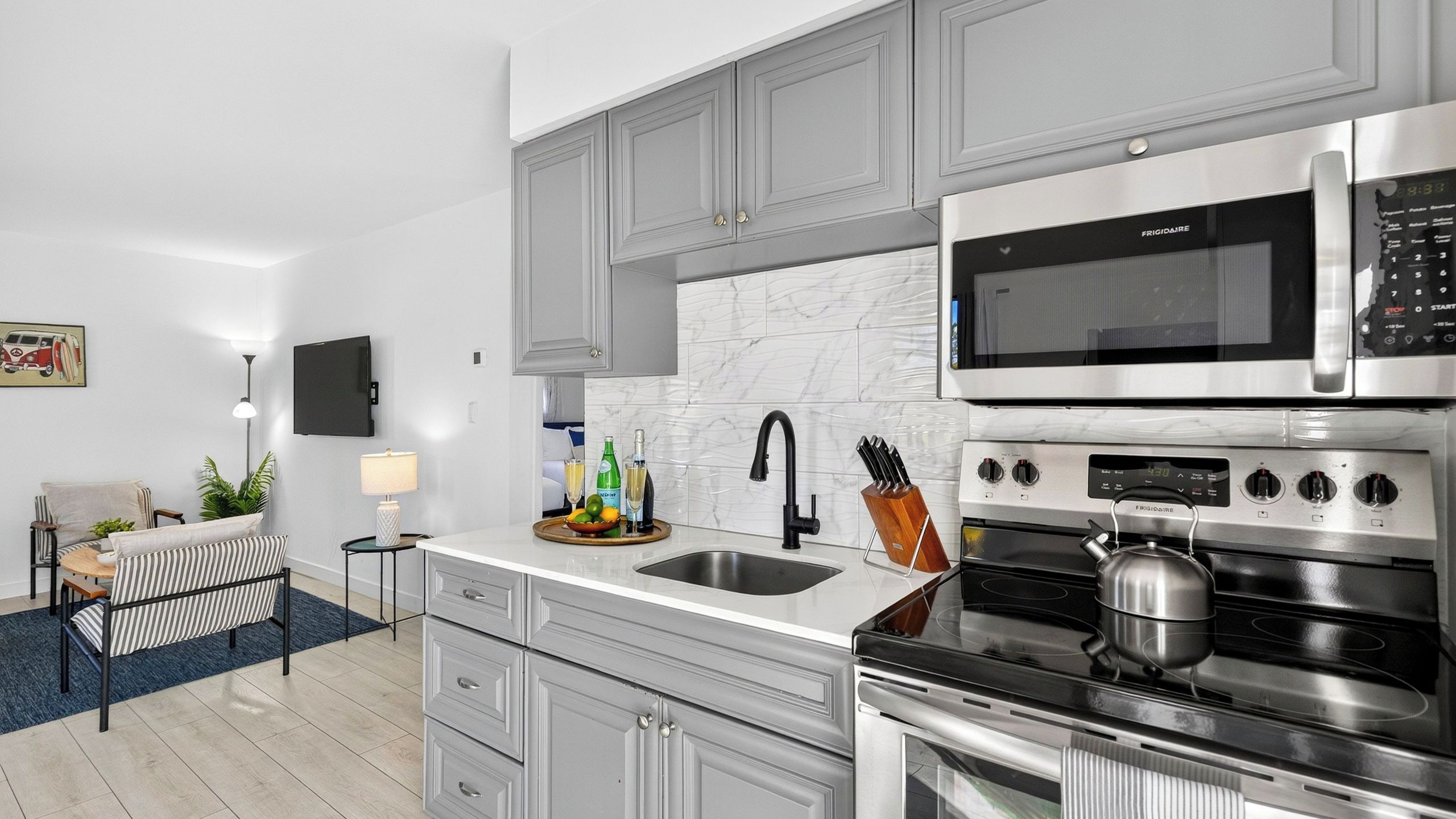 Cozinha moderna com eletrodomésticos de aço inoxidável, armários cinza e painel de backplash de mármore.